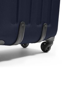 Námořnický hardshell kufr se strukturovaným povrchem, výraznými drážkami a šedými plastovými akcenty; má hladké černé kola pro snadnou mobilitu.