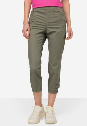 Olivgrüne Cargo-Hosen mit elastischem Bund, knöchellang und mit Seitentasche. Hergestellt aus glattem, leichtem Stoff. Kombiniert mit beigen Sneakers.