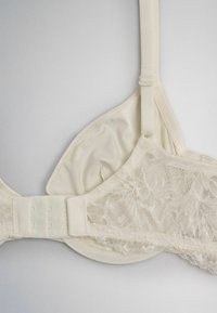 Cream-colored lace bra with adjustable straps and hook-and-eye fastening, shown flat on a light background.