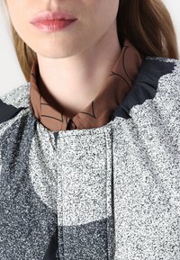 Svart och vit mönstrad blus med en kontrasterande brun skjorta med krage under; mjuka texturer med synliga knappar och veck.