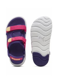 Violetit sandaalit, joissa on vaaleanpunaiset tarranauhat, verkkomateriaali ja kuvioitu valkoinen kumipohja, jossa on aaltoilukuviota ja Puma-logo.