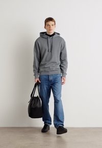 Grijze hoodie met een voorzak, gecombineerd met blauwe jeans. Een zwarte tas en schoenen maken de casual outfit compleet.