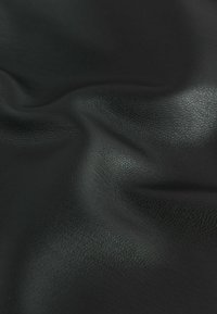 Schwarzes strukturiertes Leder mit einer glatten Oberfläche, das subtile Falten und reflektierende Eigenschaften aufweist, was auf Weichheit und Flexibilität hinweist.