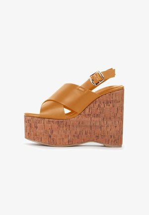 Sandali platform beige con tacco in sughero. Presentano cinghie incrociate opache e una fibbia regolabile alla caviglia. Texture della superficie liscia.