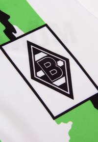 Wit shirt met groene accenten, voorzien van een zwart diamanten logo met de letter "B" en een ontwerp van een voetballetje in het midden.