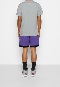 Gray crewneck t-shirt, purple mesh athletic shorts with black trim, and gray high-top sneakers featuring red accents and logo on the back.