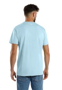 Hellblaues Baumwoll-T-Shirt mit kurzen Ärmeln und Rundhalsausschnitt. Verfügt über ein kleines "SPITZUB"-Logo auf der Rückseite, hat eine glatte Textur und eine lockere Passform.