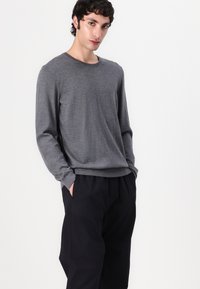 Pull gris à manches longues en matière douce avec un col rond, associé à un pantalon noir ample. Design simple, sans motifs.