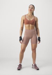 Bronzen sporttop en bijpassende hooggetailleerde shorts, gemaakt van rekbare stof. Zwarte vingerloze handschoenen en grijze sneakers maken de outfit compleet.
