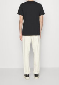 Czarna bawełniana koszulka, krótki rękaw, okrągły dekolt, w zestawieniu z jasnymi, luźnymi spodniami i czarnymi butami, widok od tyłu.