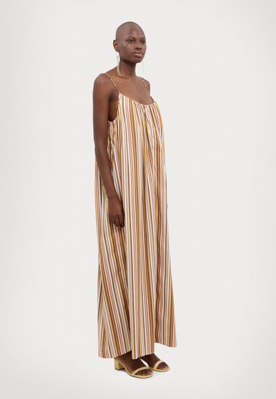 Vestido maxi a rayas en amarillo, marrón y blanco. Corte suelto con tirantes finos y escote fruncido. Combinado con sandalias de tacón bloque en color beige.