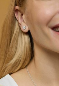 Pendientes de plata con una pequeña perla, con un diseño geométrico. Textura suave con un acabado brillante, sujetos al lóbulo de la oreja.
