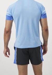 Jasnoniebieska koszulka sportowa z krótkimi rękawami, o teksturowanej tkaninie, oraz ciemne szorty z niebieskimi akcentami po bokach i białym wykończeniem, widok z tyłu.