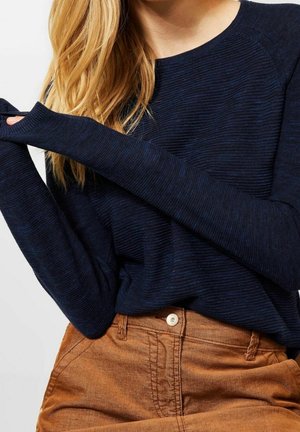 Marineblaues Langarm-Strickoberteil mit gerippter Struktur und rundem Ausschnitt, kombiniert mit braunen Cordhosen mit Knopfverschluss.