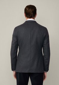 Blazer in lana grigio scuro con rever stretti, spacco posteriore e toppe sui gomiti, caratterizzato da una vestibilità sartoriale e dettagli dei bottoni coordinati sulle maniche.