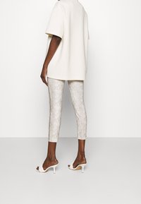 Oversized cream t-shirt, textured snake-print ankle-length pants in beige and gold tones, paired with white heeled mules.