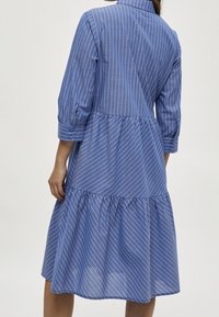Abito a righe blu con maniche a tre quarti, colletto e orlo a volant. Realizzato in un tessuto leggero, presenta righe verticali e orizzontali.