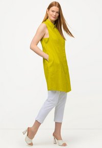 Vestido sin mangas abotonado en un brillante verde lima, con bolsillos laterales. Combinado con pantalones cortos blancos y tacones blancos destalonados.