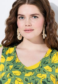 Haut sans manches en coton avec un fond vert et un motif de citrons jaunes. Présente un décolleté en V et des boucles d'oreilles texturées.