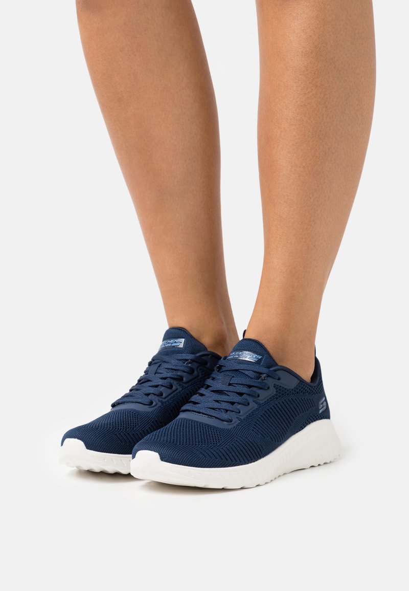 Scarpe sportive blu navy con upper in rete, design testurizzato, suola bianca e chiusura con lacci, che mostrano una struttura leggera e traspirante.