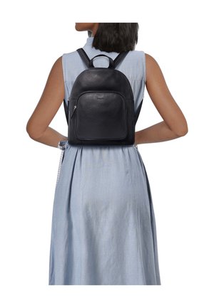 Schwarzer Leder-Rucksack mit glatter Oberfläche, Tragegriff oben, verstellbaren Gurten und einer vorderen Reißverschlusstasche. Wird zu einem hellblauen Kleid getragen.