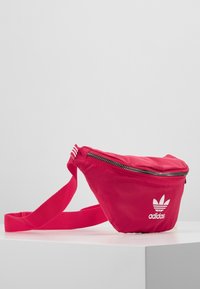Rosa Adidas midjeväska med dragkedjeöppning, justerbar rem och ikonisk logga. Tillverkad av lätt material med en slät yta.