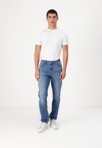 Blugi din denim albastri, cu croi drept, cinci buzunare și cusături contrastante. Purtați cu un tricou alb fitted și adidași albi.