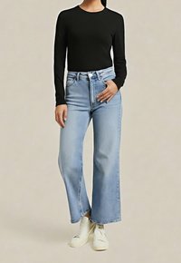 Černý top s dlouhým rukávem a kulatým výstřihem, spárovaný s vysokým pasem, světle modrými širokými džínami a bílými teniskami.