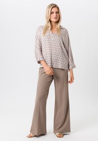 Leichte, kurzärmlige Bluse mit geometrischem Muster in Beige und Weiß, kombiniert mit beige, hoch taillierten, weit geschnittenen Hosen. Glatte Textur.