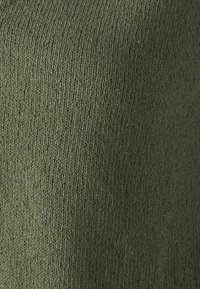 Zbliżenie na oliwkowozieloną dzianinę, ukazujące drobne, teksturowane przeszycia i miękki materiał.