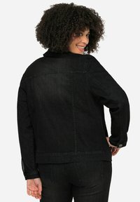 Veste en denim noir avec une coupe classique, dotée de fermetures à boutons, d'une couture au niveau de la poitrine et d'une texture lisse. Stylée avec des poches latérales.