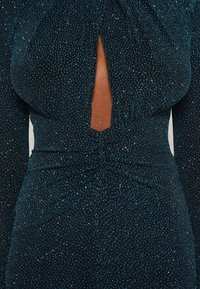 Schwarzes Kleid mit glitzernden blauen Akzenten, langen Ärmeln, einem Schlüssel-ausschnitt an der Brust und gerafftem Stoff an der Taille.