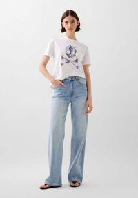 Hvid bomulds t-shirt med et farverigt kranium og korslagte knogler grafik, parret med lyseblå brede bukser med høj talje.