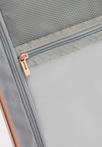 Primer plano del interior de una maleta gris que muestra un bolsillo de malla con cremallera y un tirador de cremallera en color oro rosa con la etiqueta "WITTCHEN."