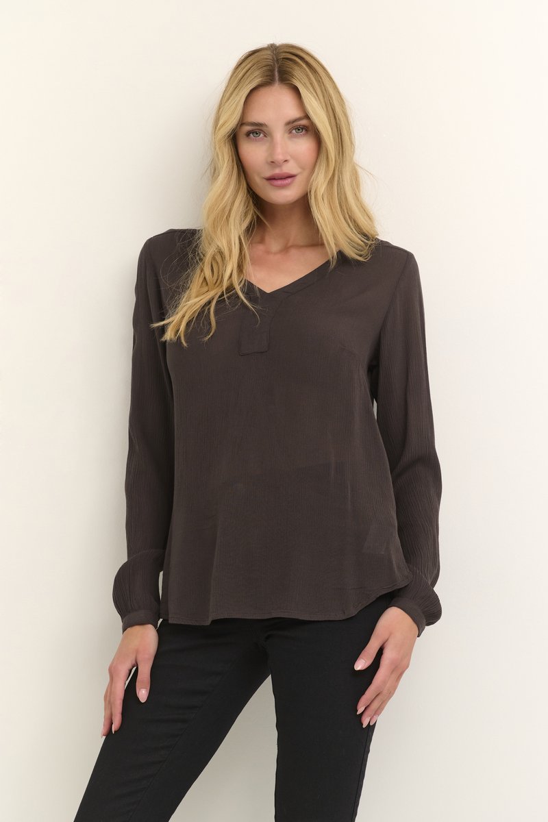 Blouse marron foncé à manches longues avec un décolleté en V et un tissu légèrement texturé ; coupe ample avec des manches à boutons et un ourlet incurvé.