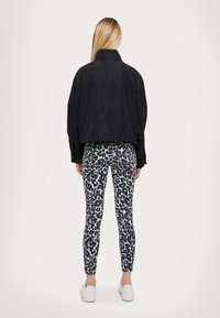 Veste noire raccourcie à col montant, associée à des leggings gris moulants ornés d'un imprimé léopard noir, et des baskets blanches.