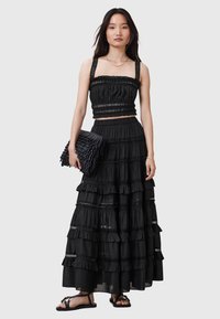 Robe noire à volants superposés, avec un buste élastique et des accents en dentelle ; assortie à une pochette noire texturée et des sandales plates.