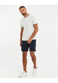 T-shirt gris clair à manches courtes avec des bordures bleu marine, associé à un short bleu marine texturé. Baskets blanches. Design minimaliste avec un petit logo.