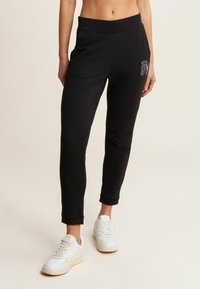 Pantalons de sport noirs avec une coupe fuselée, fabriqués dans un matériau doux, dotés d'une taille élastique et d'un petit détail décoratif sur la hanche.