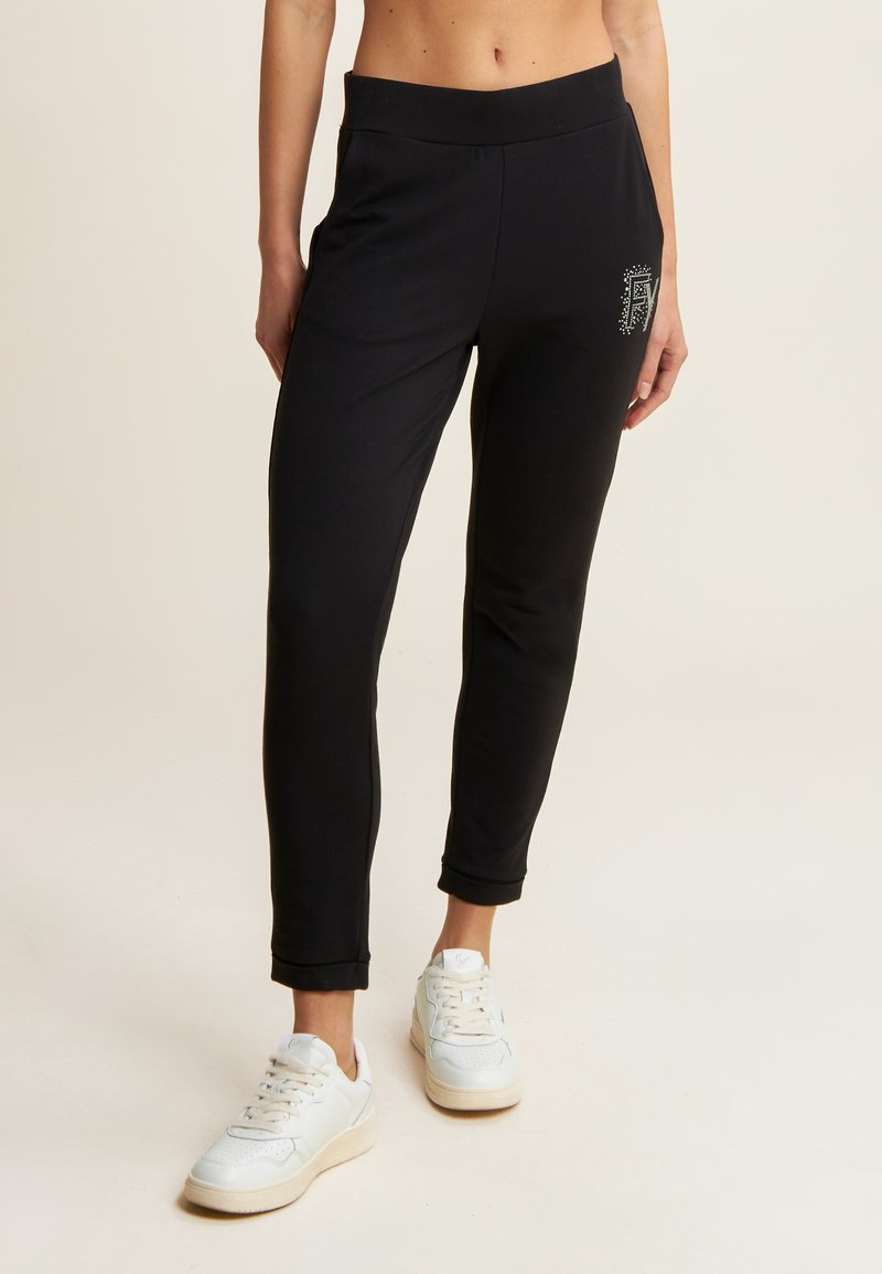 Pantalons de sport noirs avec une coupe fuselée, fabriqués dans un matériau doux, dotés d'une taille élastique et d'un petit détail décoratif sur la hanche.