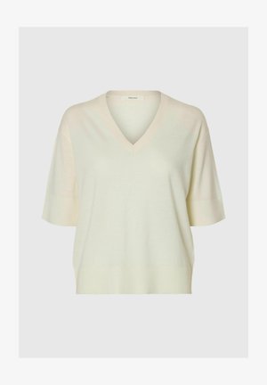 Maglione lavorato a maglia color crema con maniche corte, scollo a V, vestibilità ampia e polsini e orlo a coste su sfondo semplice.