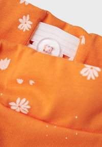 Orange cotton fabric featuring white daisy patterns, with a white elastic waistband and a button detail at the top.