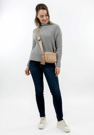 Beige crossbody bag with a textured finish, two zippered compartments, and a tassel accent. Paired with a gray sweater and blue jeans.