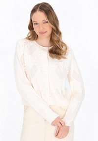 Cardigan color crema con maglia texture, caratterizzato da motivi diagonali e borchie in rilievo. Ha un collo rotondo e chiusura a bottoni.