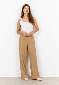 Beige gerippte weit geschnittene Hose, kombiniert mit einem taillierten weißen Tanktop, das eine glatte, weiche Textur und eine lässige Silhouette aufweist.
