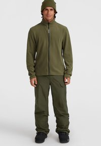 Grüne Fleecejacke mit hohem Kragen und Frontreißverschluss, kombiniert mit passenden grünen Cargo-Hosen und schwarzen Schneestiefeln.