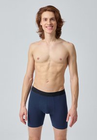 Boxers-briefs bleu marine avec une ceinture élastique noire, fabriqués à partir d'un tissu lisse et extensible. Le design présente une forme ajustée et des coutures plates.