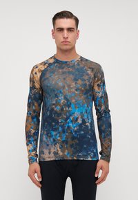 Cămașă cu mânecă lungă, având un model tie-dye în nuanțe de albastru, maro și negru. Materialul pare neted, cu un design ajustat și mâneci raglan.