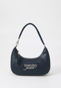 Μικρή μπλε σκούρα τσάντα ώμου με έναν ιμάντα, ασημένιο φερμουάρ και το λογότυπο "tommy jeans" σε ασημί γράμματα στο μπροστινό μέρος.
