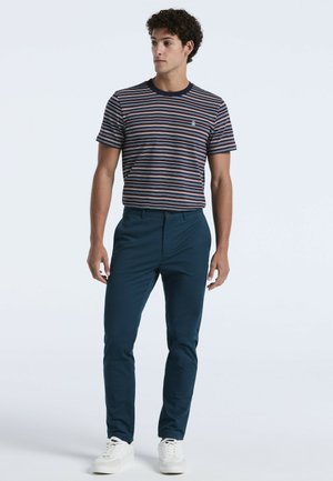 Gestreiftes kurzärmliges T-Shirt in Marineblau mit mehrfarbigen Streifen, kombiniert mit eng anliegenden, dunkelblauen Hosen und weißen Sneakers.